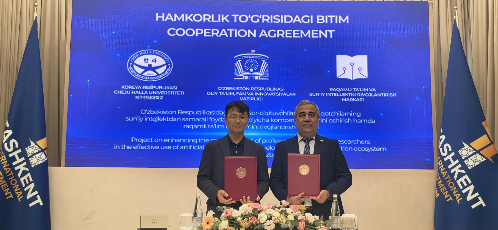 The two signatories holding the signed folders in front of the cooperation-agreement banner