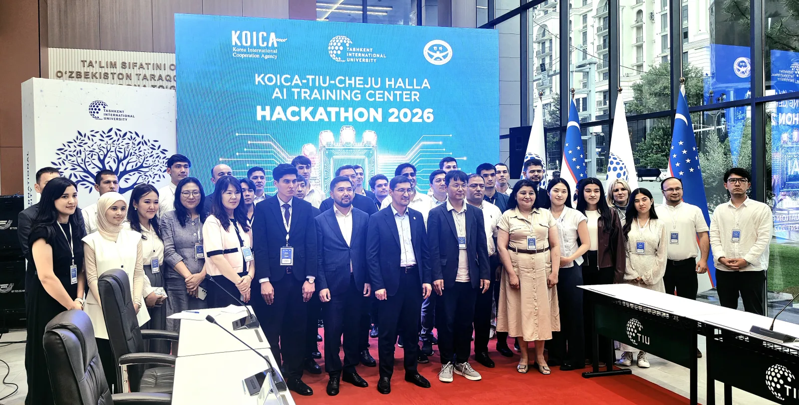 Participants and officials of the KOICA-TIU-Cheju Halla AI Training Center gathered for a group photo in front of the "Hackathon 2026" LED backdrop, with Uzbek flags, at the TIU AI campus in Tashkent
