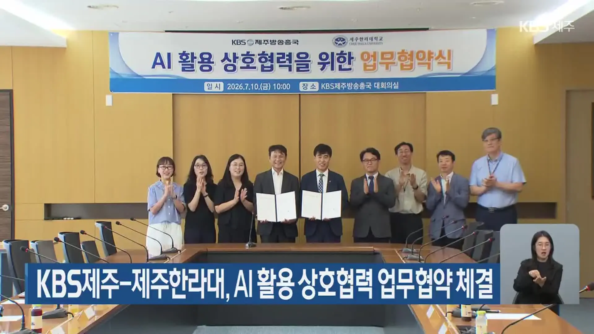 KBS Jeju's news report on the signing: nine people behind the conference table, Park Jong-in and I at center holding the open agreement folders, under a banner reading "AI 활용 상호협력을 위한 업무협약식 / 2026.7.10.(금) 10:00 / KBS제주방송총국 대회의실"