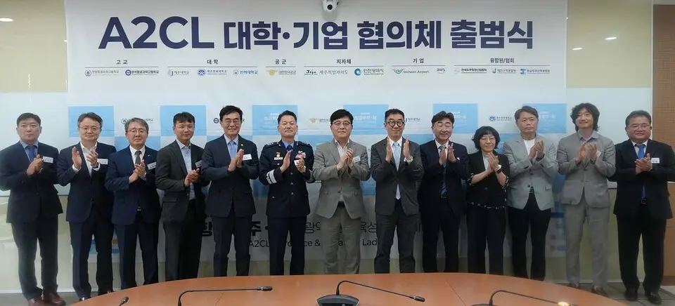 The A2CL university-industry council launch: fourteen representatives applauding in front of a banner reading "A2CL 대학·기업 협의체 출범식", the participating logos grouped above them by category into high schools, universities, the Air Force, provincial and city governments, companies, and industry associations