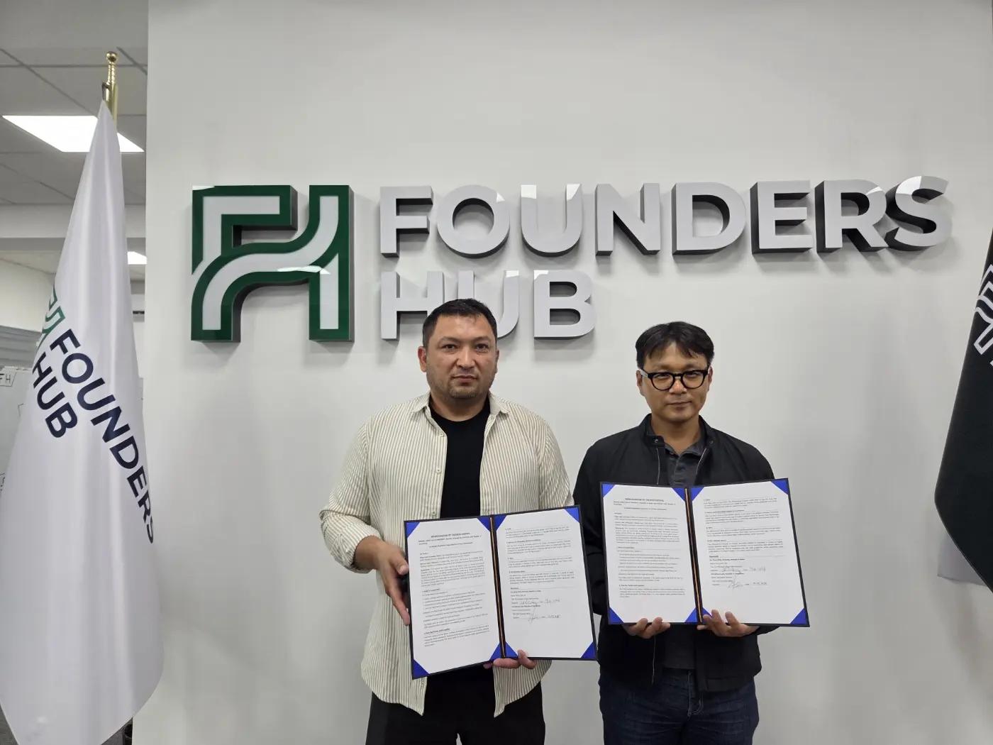 Xurshidbek Kurbanov, CEO of InFocus Labs, and Young Joon Lee holding the signed MOU in front of the Founders Hub logo wall in Tashkent