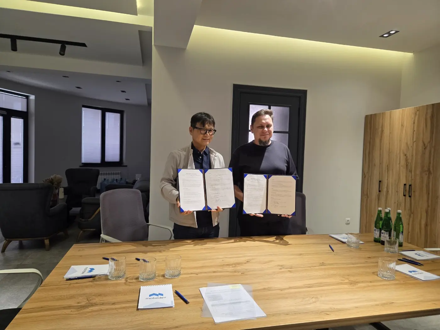 Dr. Anvar Narzullaev, CEO of Mohirdev, and Young Joon Lee holding the signed MOU folders in the Mohirdev meeting room